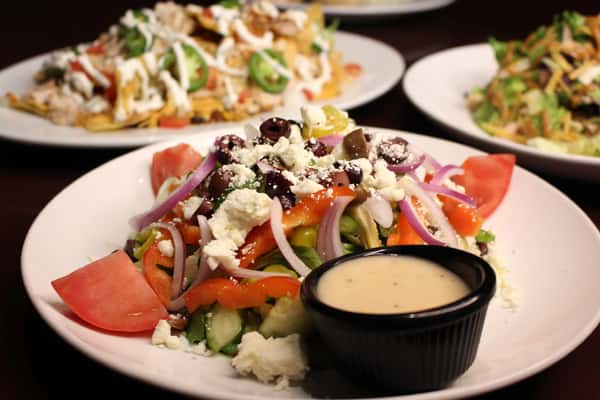 Greek-style salad with tomatoes, cucumbers, olives, and feta cheese, served with a side of dressing