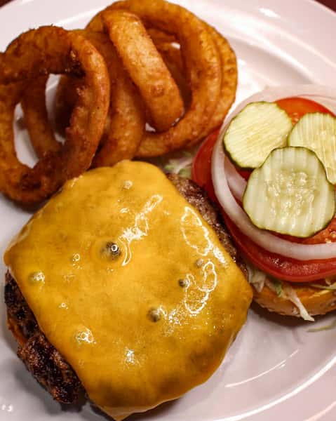 Cheeseburger topped with melted cheese, lettuce, tomato, onion, and pickles, served with onion rings