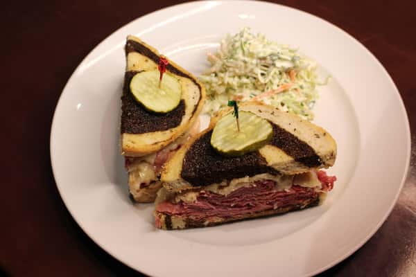 Sliced pastrami sandwich on rye with pickle spears and coleslaw