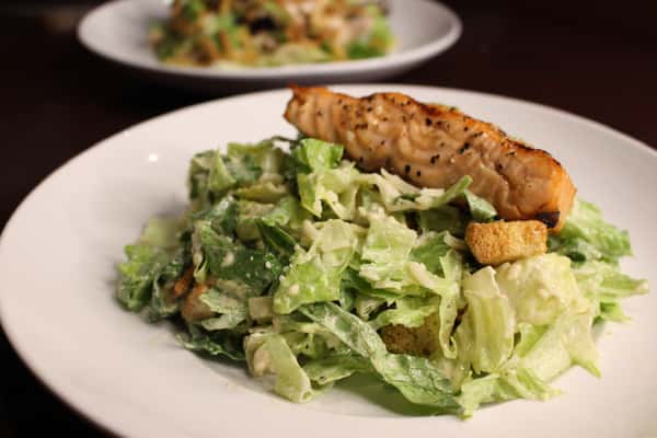 Caesar salad topped with grilled chicken skewers and croutons