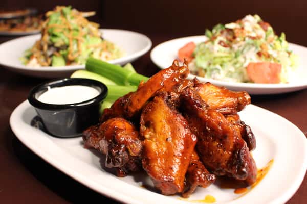 Plate of glazed chicken wings served with celery sticks and dipping sauce
