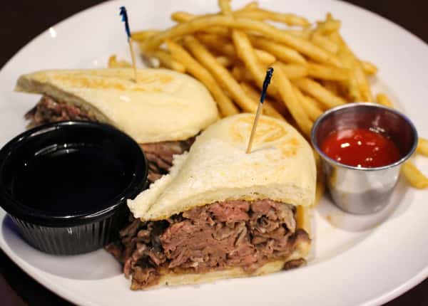 Sliced steak sandwich served with french fries and a dipping sauce