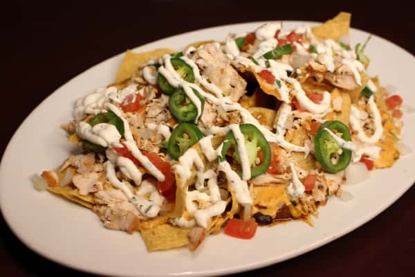 Loaded nachos topped with shredded chicken, jalapeños, and a drizzle of crema
