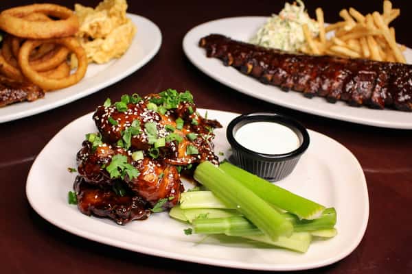 Plate of spicy glazed chicken bites with celery and dipping sauce, with ribs in the background