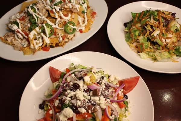 Two plates of food: tortilla chips with a fresh salad, and a mixed salad with tomatoes and cheese