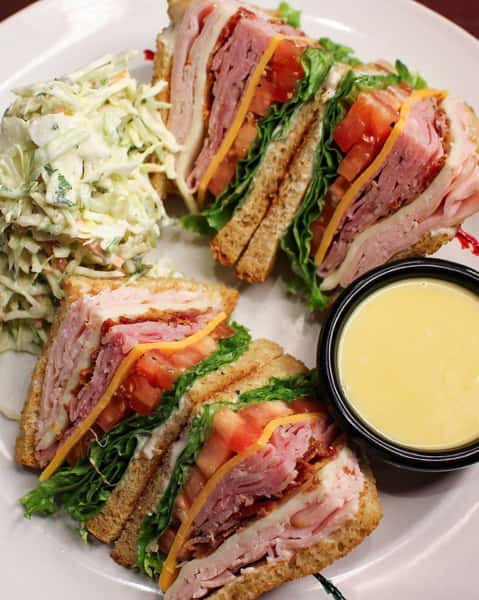 Club sandwich cut into quarters, served with a dipping sauce and coleslaw