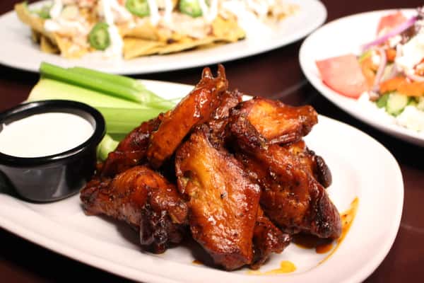 Plate of glazed chicken wings served with celery sticks and dipping sauce