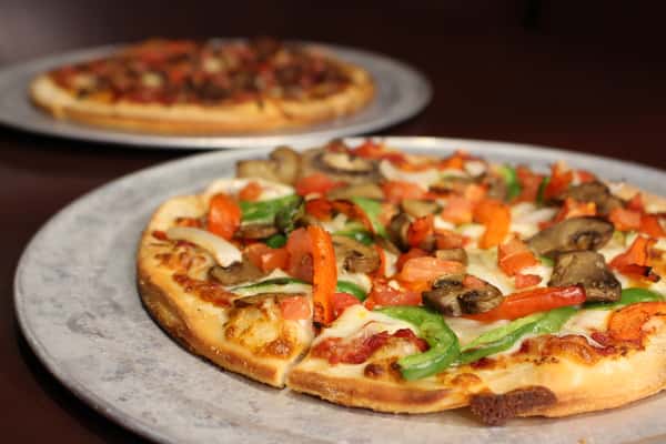 Pizza topped with fresh tomatoes and arugula, with another pizza in the background
