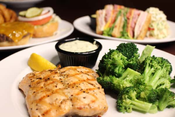 Grilled chicken breast served with steamed broccoli, a dipping sauce, and a lemon wedge