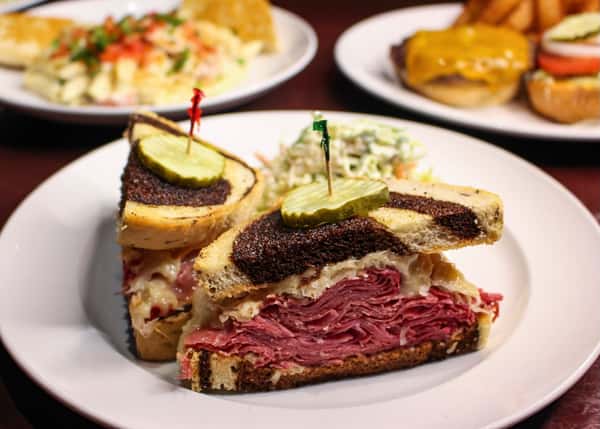 Sliced pastrami sandwich with a pickle spear, served with coleslaw