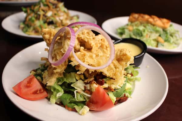 Salad topped with a fried item, red onion rings, and tomato wedges