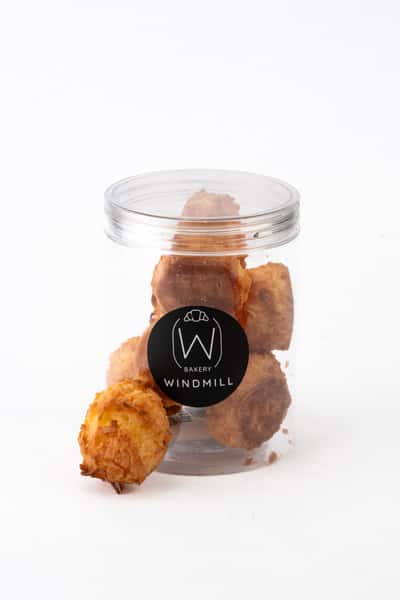 Golden-brown bite-sized pastry balls in a clear branded bakery jar, featuring crisp, flaky texture and artisan snack-style presentation on a clean white background.