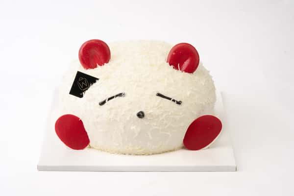 Cute bear-shaped coconut mousse cake with fluffy white texture, decorated with red chocolate accents and minimalist facial details, styled as a playful artisan bakery dessert on a clean background.