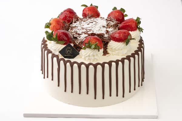 Strawberry chocolate drip cake topped with fresh strawberries, whipped cream swirls, and chocolate shavings, creating a rich and elegant bakery dessert centerpiece.