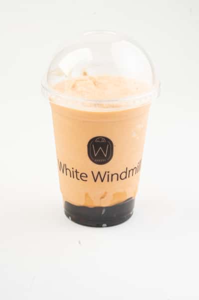 Iced milk tea or Thai-style iced tea with a dark syrup layer, served in a clear takeaway cup with dome lid, showcasing creamy orange color and modern café drink presentation.