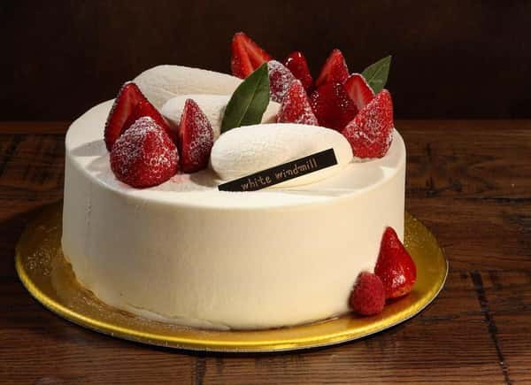 Strawberry shortcake with white frosting, fresh strawberries, and White Windmill plaque on gold cake board