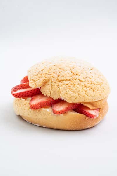 Strawberry cream bun sandwich with fresh sliced strawberries and whipped cream in a soft sweet roll, styled as a light bakery dessert on a clean background.