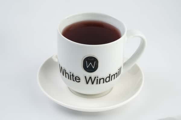 Hot black tea in a branded White Windmill ceramic cup and saucer, served on a clean white surface for a minimalist café presentation.