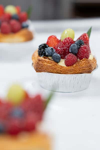 Fresh mixed berry pastry tart with flaky crust and creamy filling, topped with strawberries, blueberries, raspberries, and grapes for a vibrant bakery dessert display.