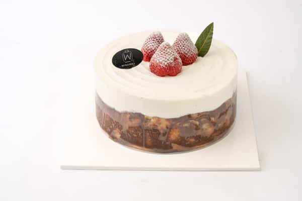 Strawberry cream cake with smooth white frosting and chocolate crunch layer, topped with powdered fresh strawberries for an elegant bakery dessert display.