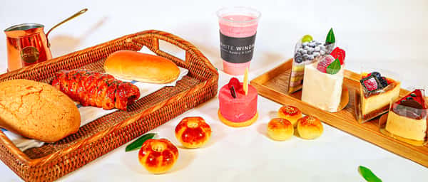 Assorted pastries and cakes with bread basket, berry cake slices, pink drink, and small buns on display