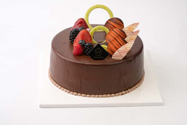Glossy chocolate mousse cake topped with fresh berries, decorative chocolate pieces, and modern pastry accents for a premium bakery dessert presentation.