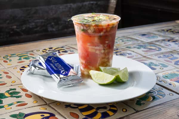 Shrimp Coktel in a plastic cup on a white plate with crackers and lime slices