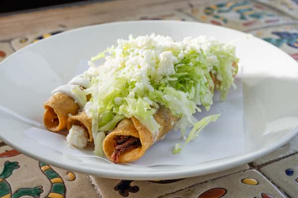 Close up of three rolled tacos topped with lettuce and cheese