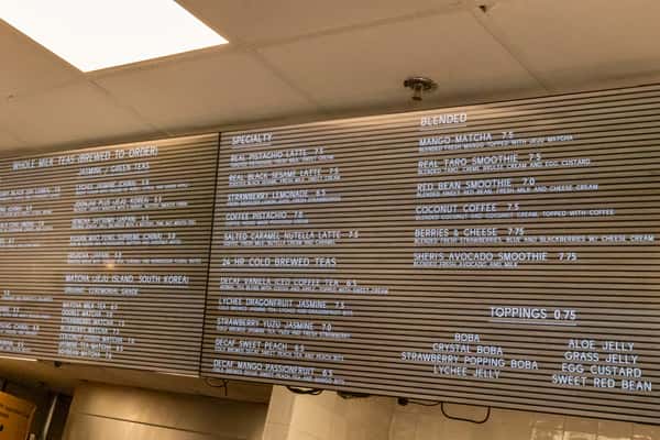 Overhead menu board featuring a wide selection of brewed teas, specialty lattes, smoothies, and customizable toppings like boba, lychee jelly, and grass jelly.