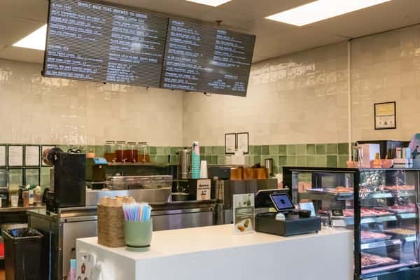 Interior counter of a modern tea shop with digital menu boards, iced tea dispensers, and a register, highlighting a clean and inviting ordering area.