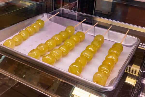 Skewers of glossy green candied grapes neatly arranged on a silver tray, showcasing a traditional Asian-style fruit snack with a shiny sugar coating.