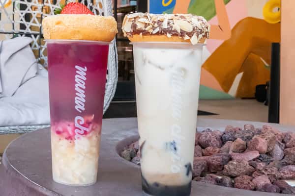 Two signature boba drinks from Mama Chai's topped with donuts—one a layered berry tea with fruit bits and a strawberry, the other a creamy milk tea with boba and a chocolate almond donut.