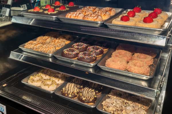 Wide view of Mama Chai's dessert case filled with assorted donuts—strawberry cream, caramel-glazed, chocolate with sprinkles, coconut, pistachio, and almond-topped varieties—perfect for sweet-tooth cravings and visually rich social media content.