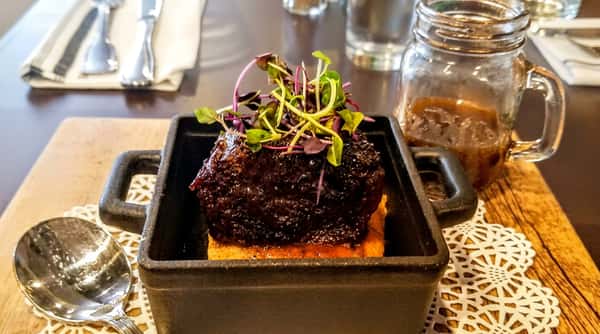 Braised short rib over polenta, topped with microgreens, served in a black cast iron dish.