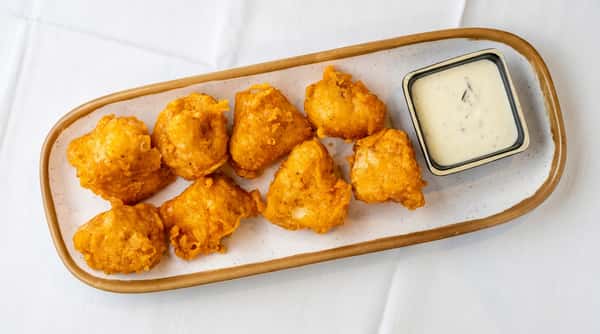 Seven golden-brown fried battered food pieces on a rectangular plate with a side of white dipping sauce.