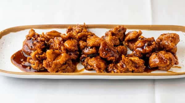 Crispy fried chicken pieces coated in a dark, glossy sauce and sprinkled with black sesame seeds on a white rectangular plate.