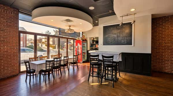 Diner interior with large windows, wooden floors, tables and chairs, a red Coca-Cola fridge, and a specials chalkboard.