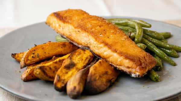Pan-seared salmon fillet with roasted sweet potato wedges and green beans on a gray plate.