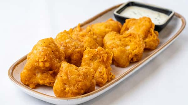 Fried fish nuggets on a white rectangular plate with a side of white dipping sauce in a black dish.