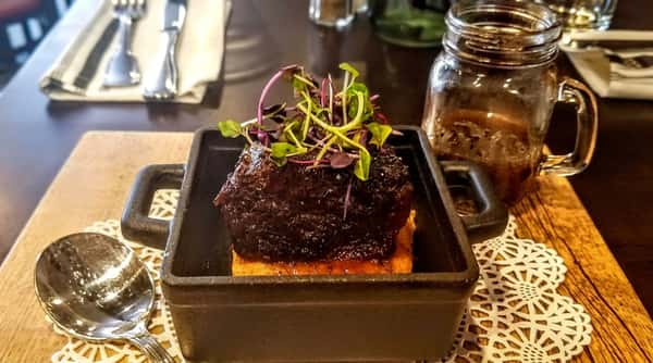 Braised short rib over polenta in a cast iron dish, topped with microgreens, next to a mason jar and spoon.