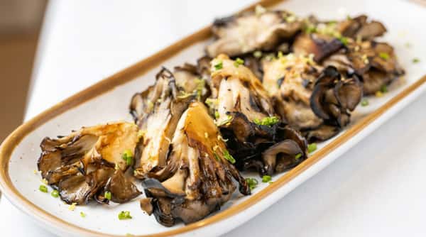 Grilled maitake mushrooms with lime zest and chopped chives on a white rectangular plate.