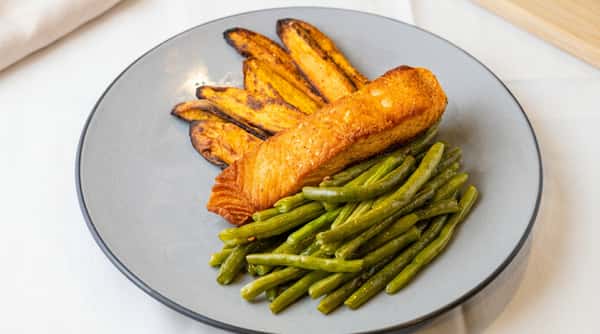 Pan-seared salmon fillet with roasted sweet potato wedges and green beans on a gray plate.