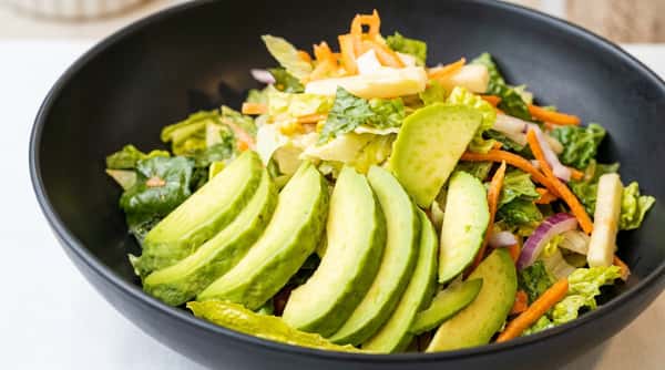 A fresh green salad in a black bowl with sliced avocado, shredded carrots, and lettuce.