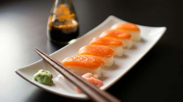 Salmon nigiri sushi on a white rectangular plate with chopsticks, wasabi, and a soy sauce bottle.