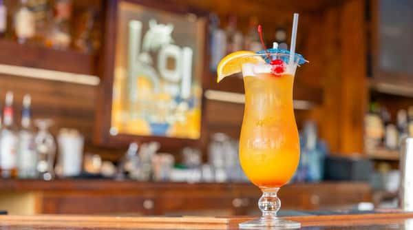 Tropical cocktail in a hurricane glass, garnished with an orange slice, cherry, and small umbrella.