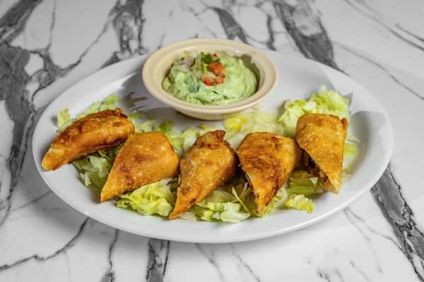 Crispy golden empanadas served on shredded lettuce with a side of creamy guacamole — crunchy Mexican appetizer perfect for sharing.