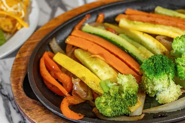 Colorful grilled vegetable fajitas served on a hot skillet with carrots, squash, bell peppers, and broccoli — a vibrant vegetarian Tex-Mex option.