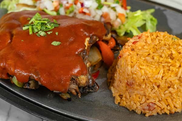 Plate of Mexican-style ribs smothered in rich red enchilada sauce, served with fluffy Mexican rice and a side of lettuce and pico de gallo.