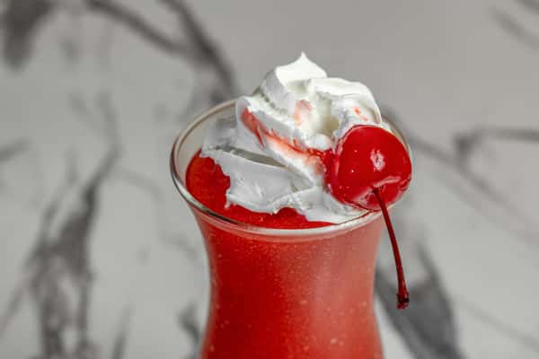 Close-up of a frozen strawberry daiquiri topped with whipped cream and a maraschino cherry, served in a curved cocktail glass — vibrant tropical drink perfect for summer vibes and happy hour menus.