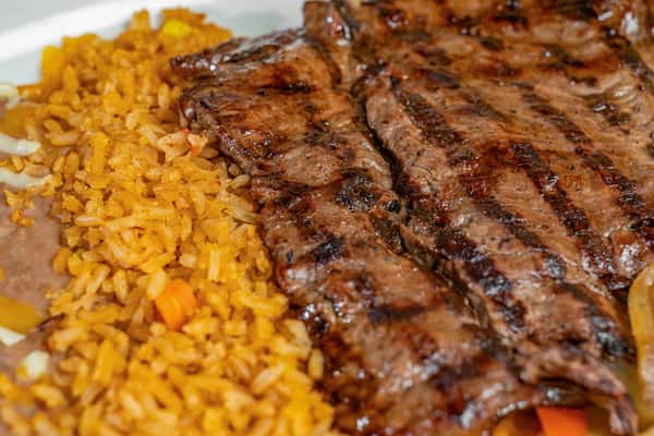 Juicy grilled carne asada steak with seared grill marks, served with refried beans and flavorful Mexican rice.